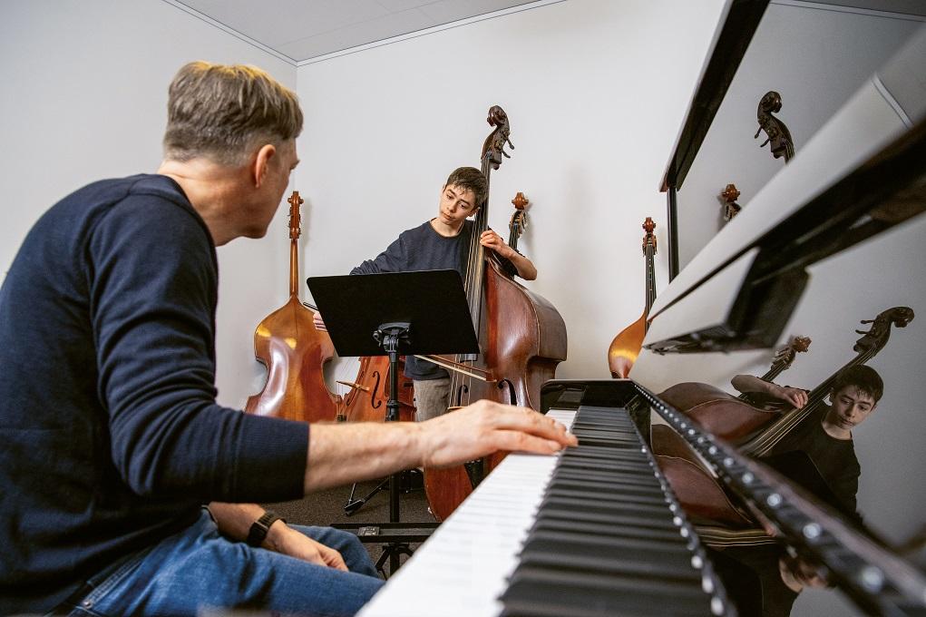 Der Lehrer sitzt am Klavier und begleitet einen Knaben am Kontrabass.