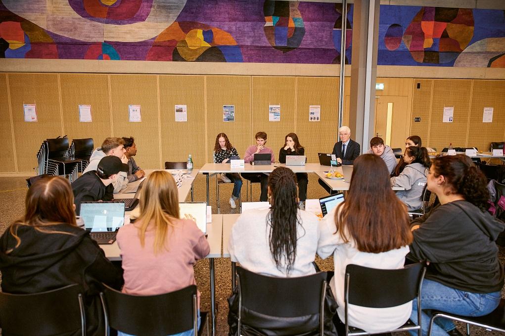 Schülerinnen und Schüler sitzen an Pulten im Kreis und debattieren..