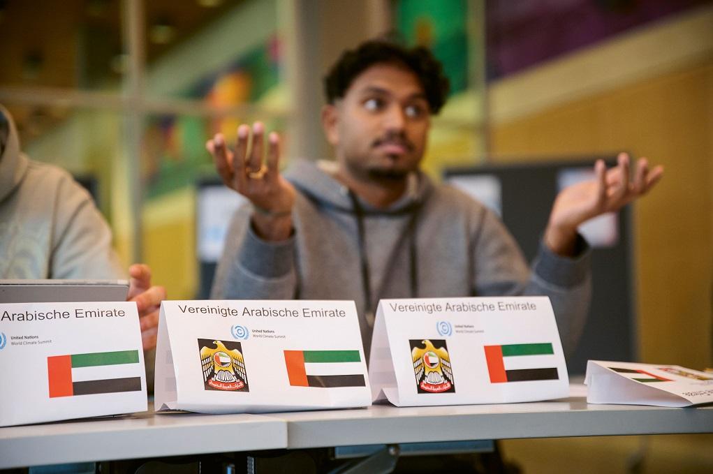 Ein Jugendlicher sitzt hinter dem Länderschild der Vereinigten Arabischen Emiraten