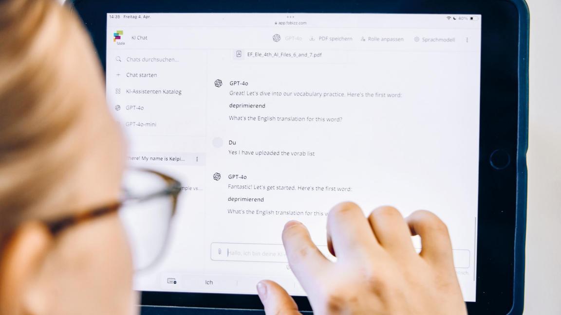 Eine Schülerin tippt auf ihren Bildschirm, auf dem eine Konversation mit Dialogfeld zu sehen ist.  