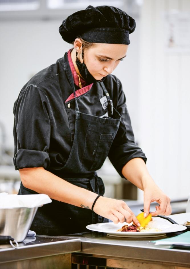 Eine junge Frau mit Schürze richtet konzentriert ein Gericht an auf einem Teller