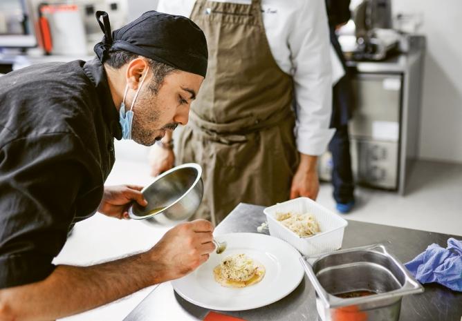Ein junger Mann mit Kopfbedeckung richtet konzentriert ein Menü an auf dem Teller