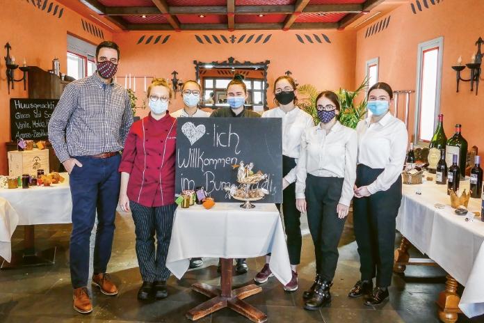 7 Personen mit Corona-Schutzmaske und Service-Tenü stehen in einem Wirtshaussaal