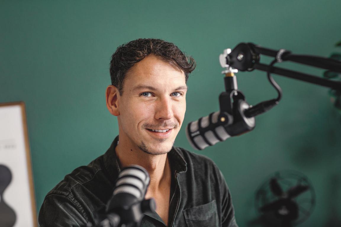 Junger Mann schaut in die Kamera und hat zwei Podcast-Mikrofone vor sich