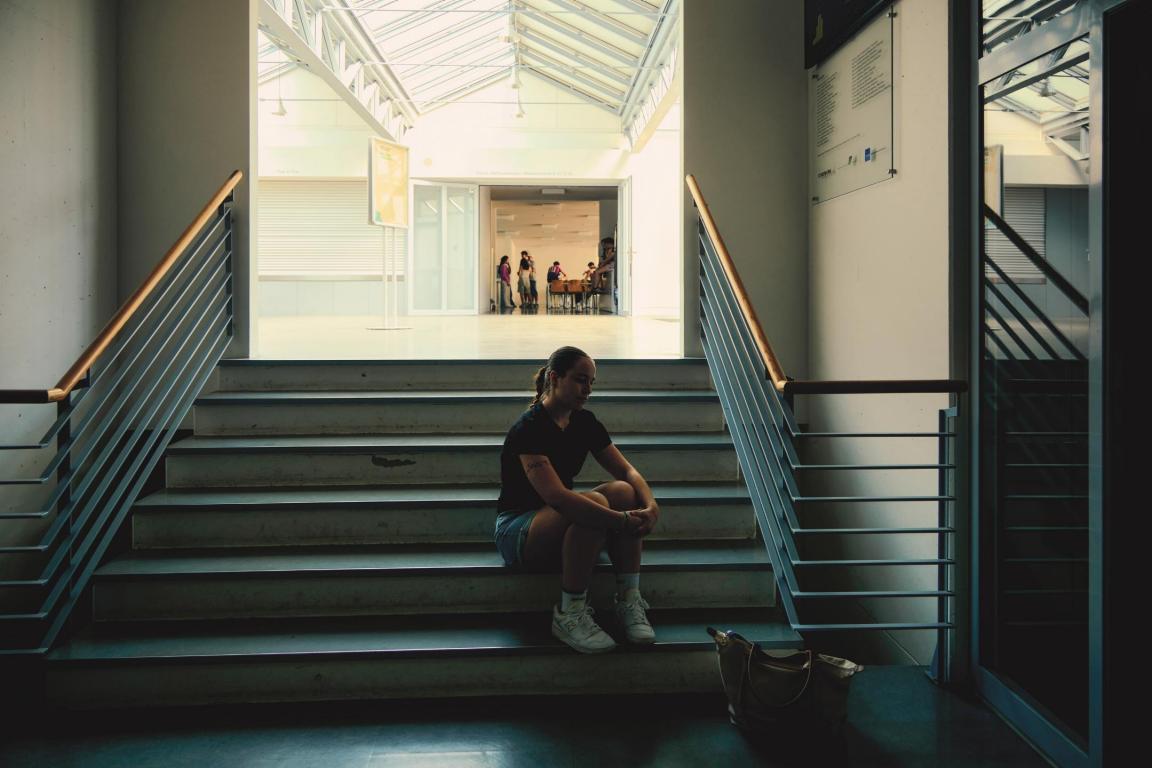 Jugendliche sitzt auf einer Treppe, die zur Mensa hochführt und schaut in die Ferne
