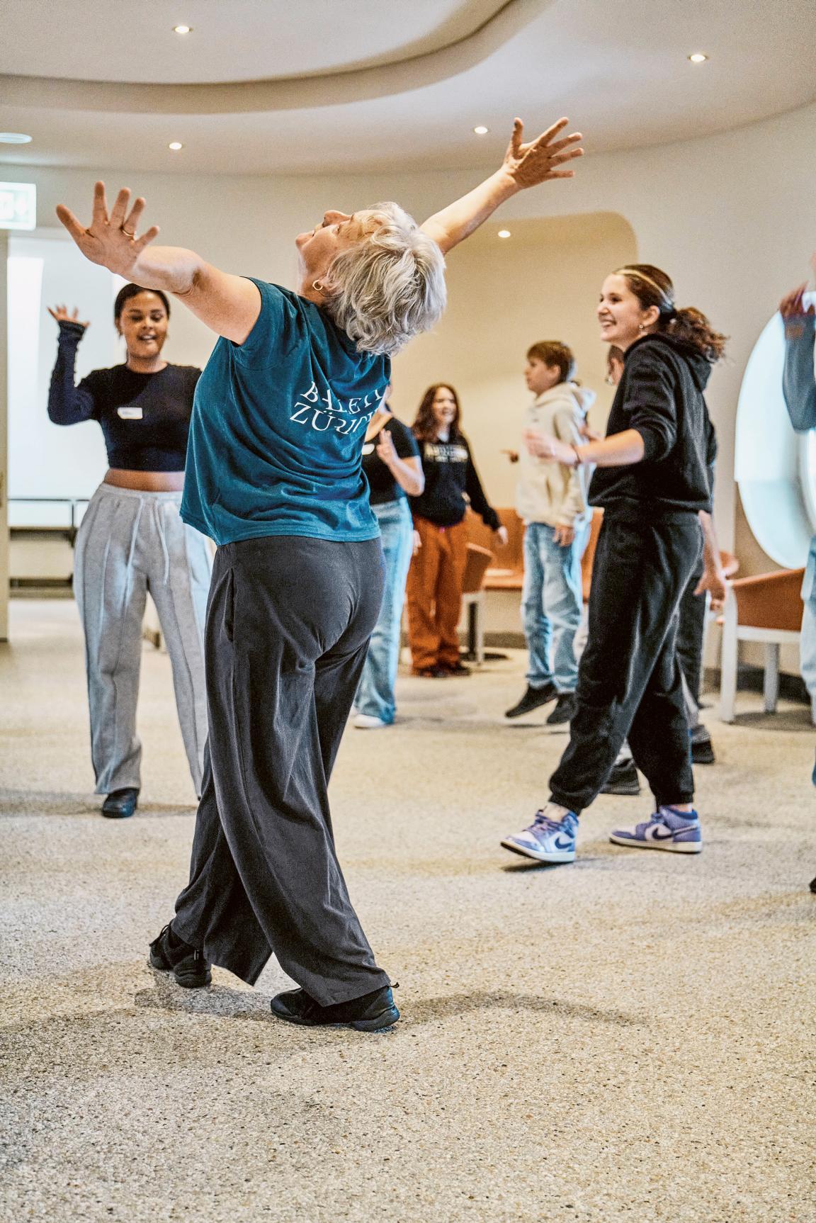 Eine Frau streckt die Arme weit von sich. Die jungen Mädchen um sie herum, machen es ihr nach.