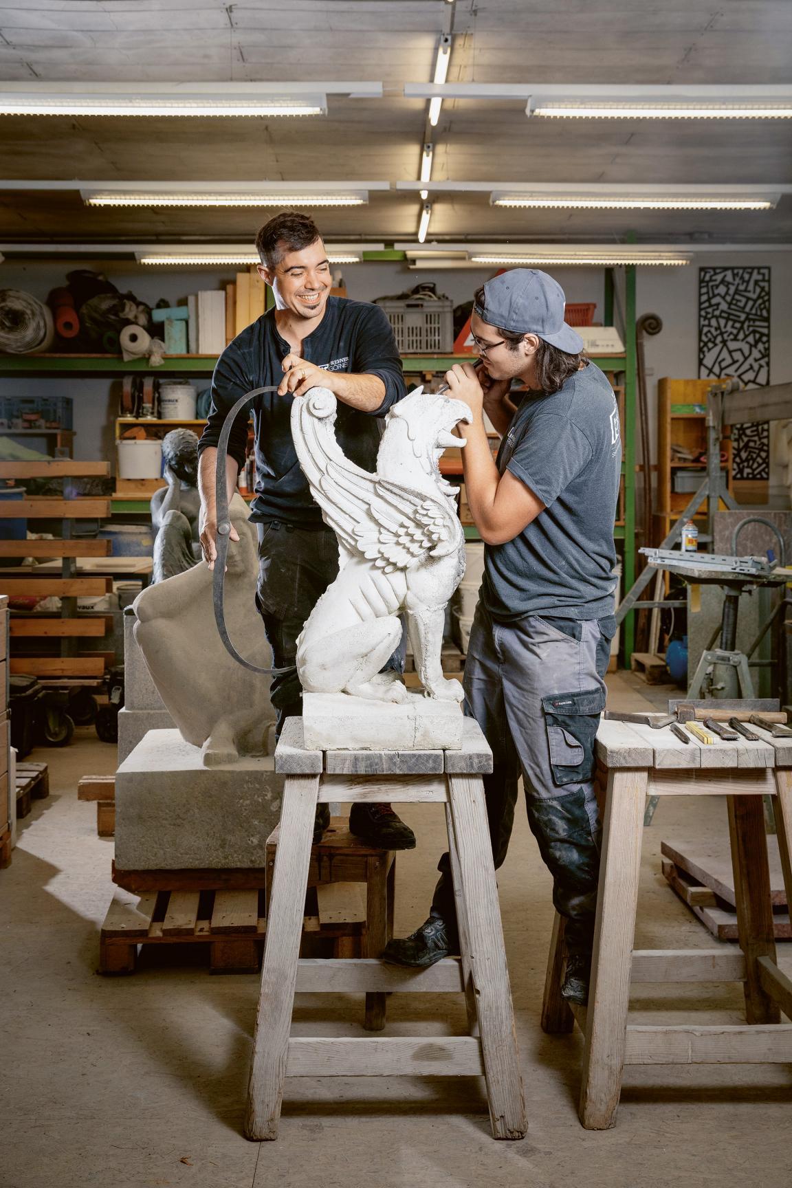 Ein Mann arbeitet an einer Steinbüste und wird von einer zweiten Person dabei unterstützt.