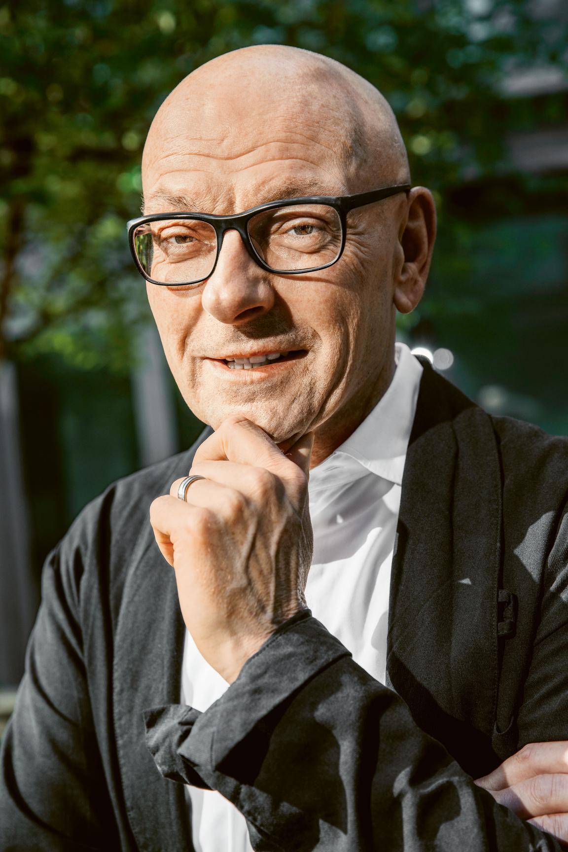 Otto Bandli in Denkerpose. Er hat eine Glatze und trägt eine Brille mit schwarzem Gestell. Er trägt eine dunkle Jacke über einem grauen Hemd.