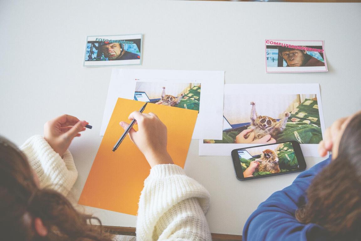 Schülerin von oben fotografiert, sie arbeitet an einem Schreibtisch. Auf dem Tisch liegen Bilder und eine Arbeitsmappe 