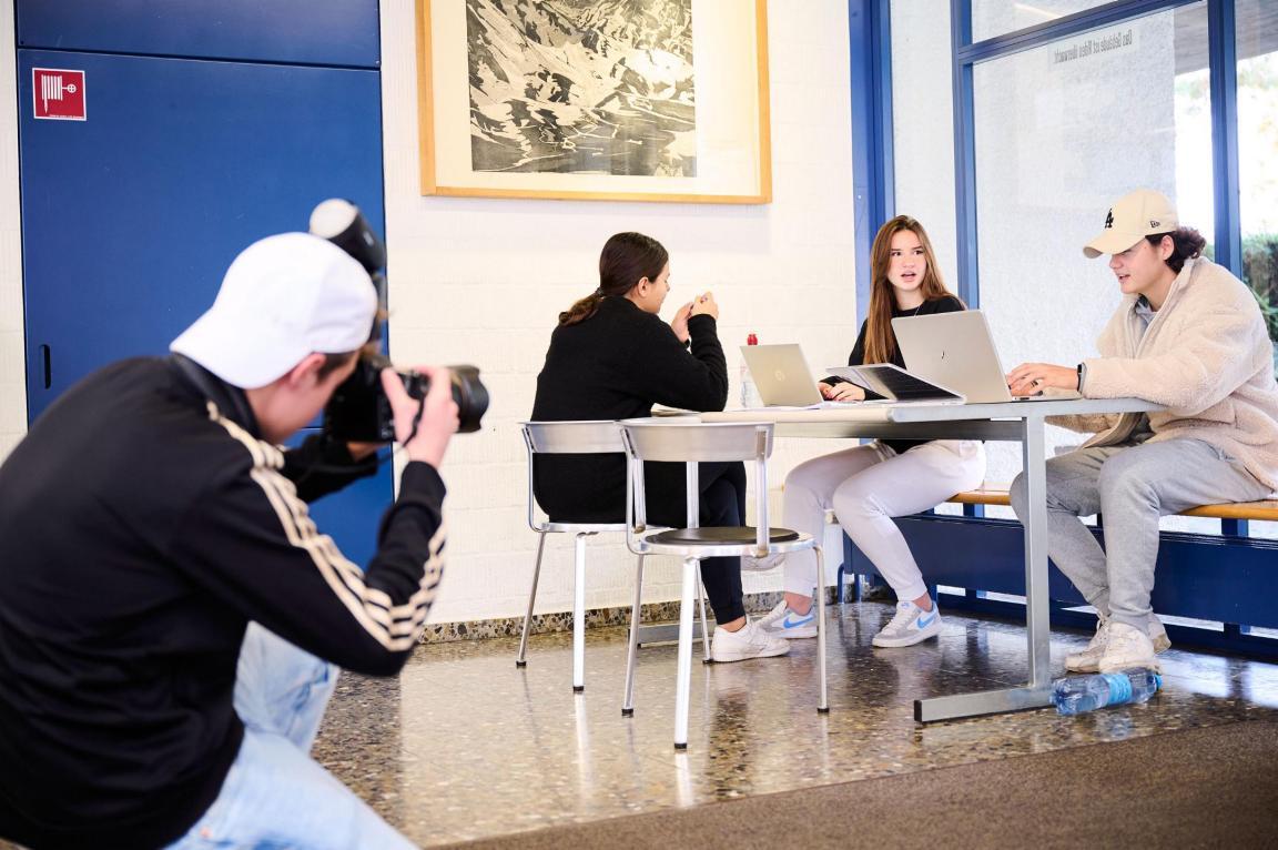 Am Tisch sitzende Jugendliche werden von einem Klassenkameraden fotografiert