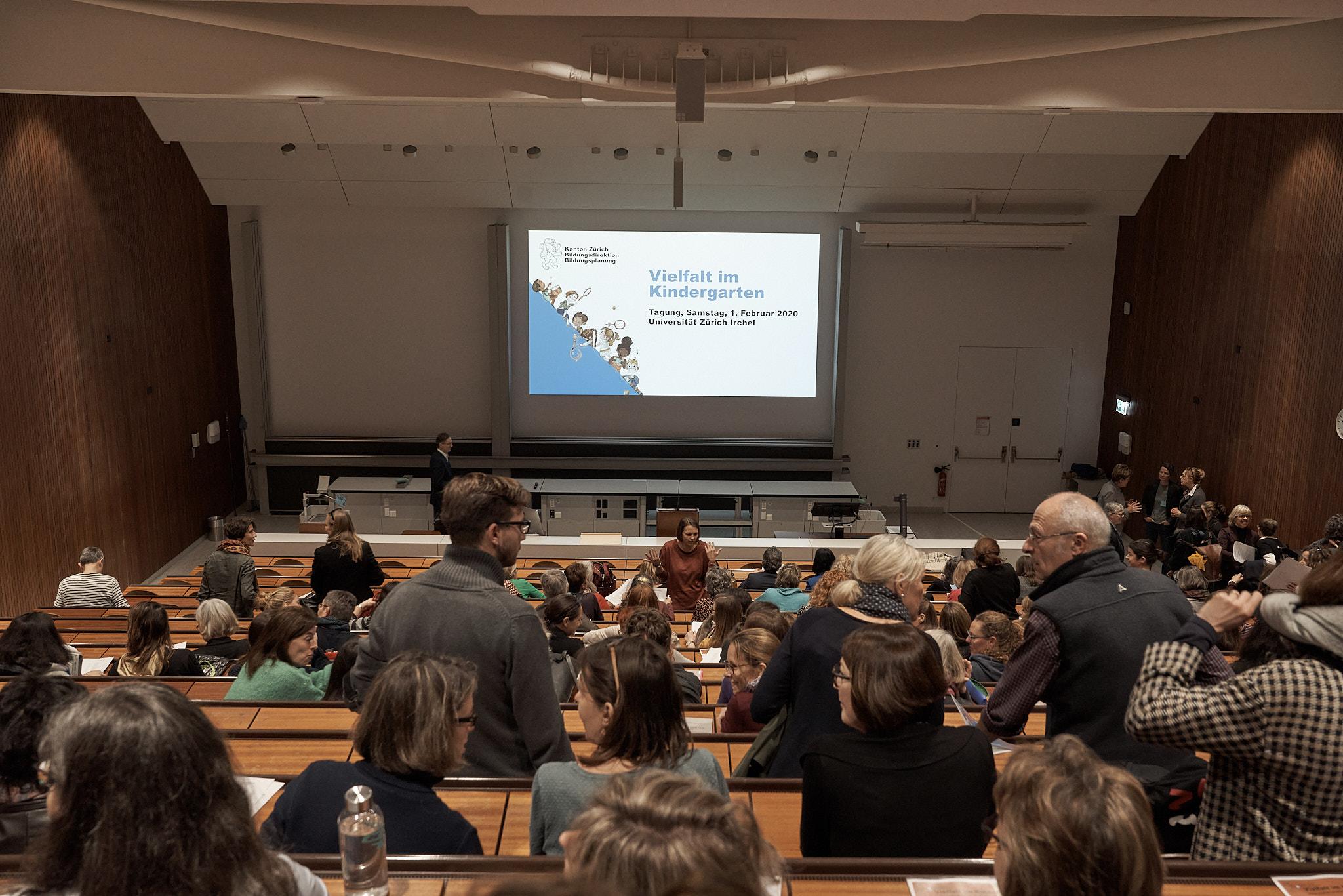 Die Besucher/innen nehmen im Plenumssaal der Veranstaltung platz.