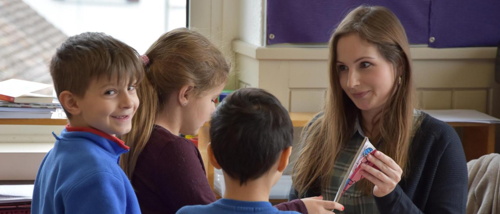 Drei Primarschüler stehen vor dem Pult der Lehrein.