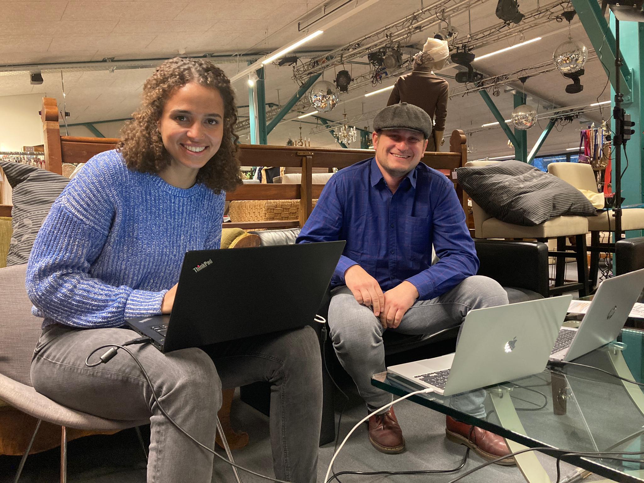 Eine lachende Frau und ein lachender Mann auf Sofa mit drei Laptops im Vodergrund