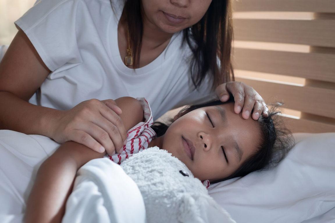 Eine Mutter hält die Hand auf die Stirn ihrer schlafenden Tochter.