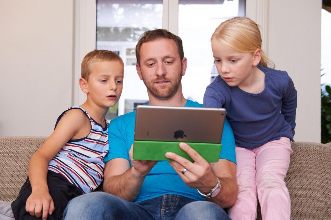 Ein Vater mit zwei Kindern nutzt das Internet auf einem Tablet.