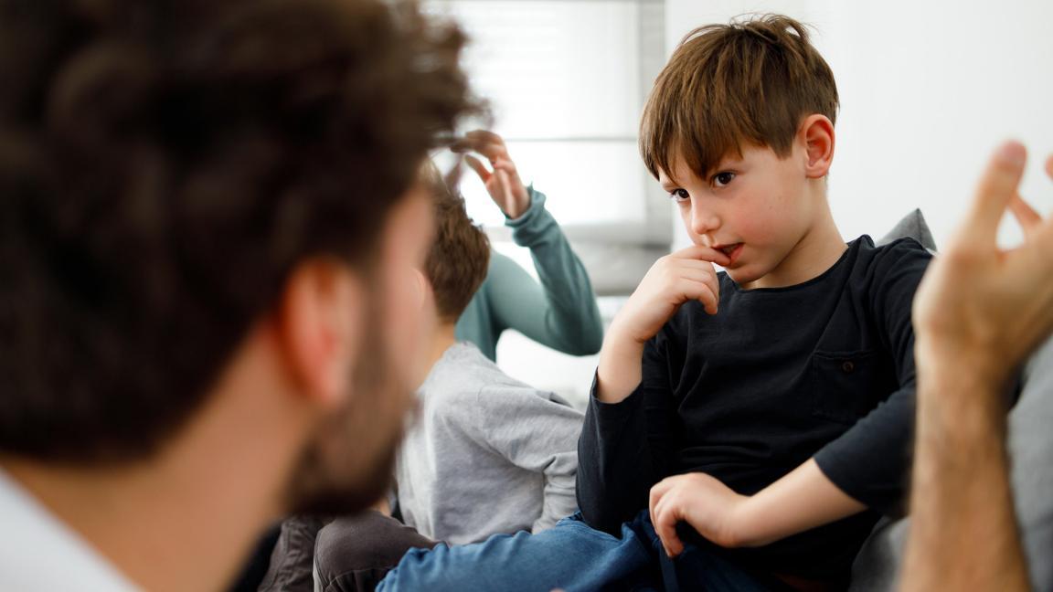 Ein Junge sitzt nachdenklich auf einem Sofa und hört einem Erwachsenen zu, der mit ihm spricht.