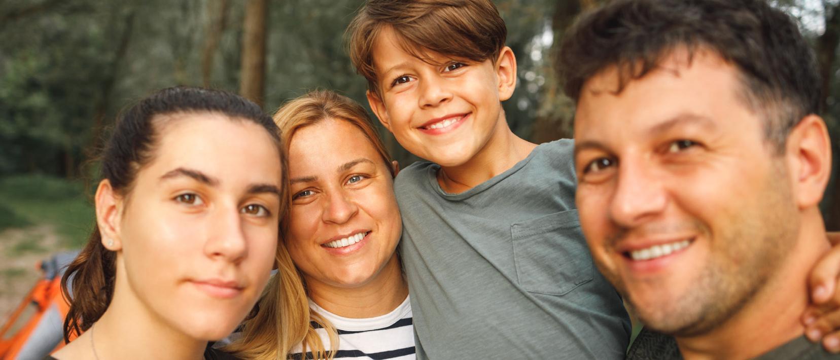 Eine glückliche, vierköpfige Familie macht draussen im Grünen ein gemeinsames Selfie.