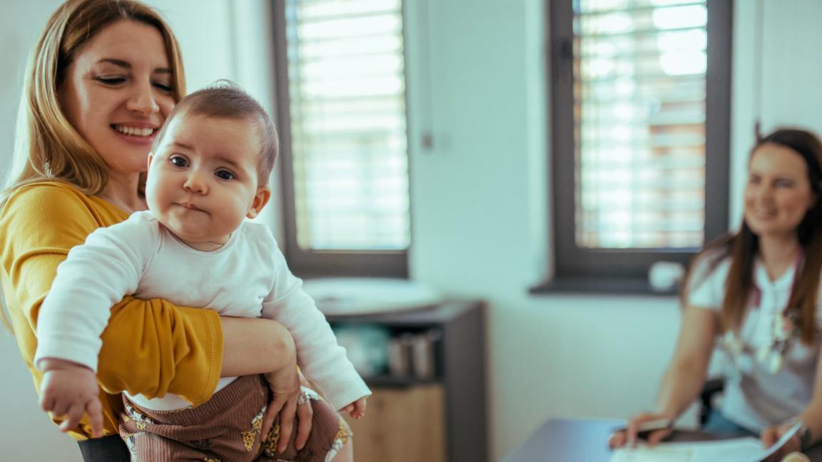 Eine Mutter sitzt lächelnd mit ihrem Baby auf dem Schoss in einem Beratungsgespräch.