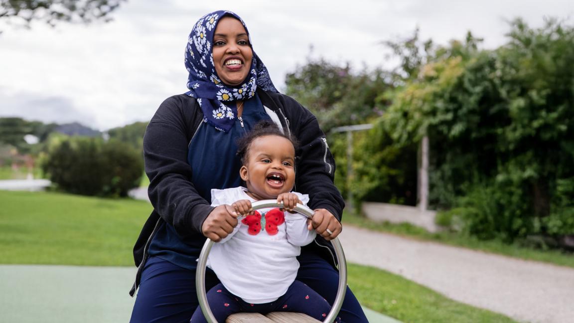 Eine Mutter spielt fröhlich mit ihrem Kind auf einem Spielplatz im Grünen.