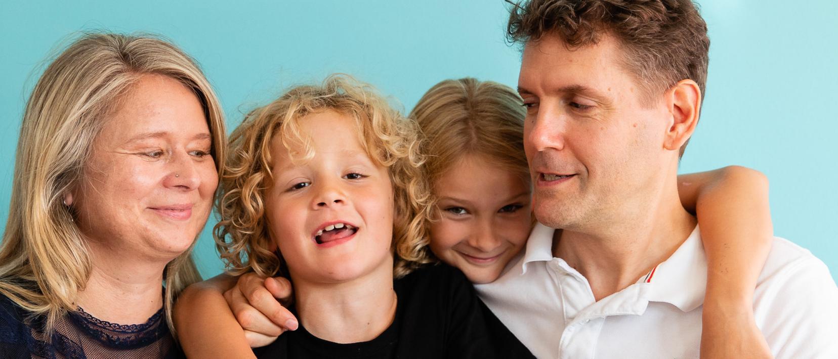 Eine fröhliche Familie hält sich eng umschlungen und lächelt in die Kamera.