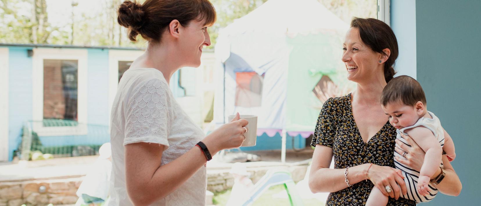 Zwei Frauen unterhalten sich. Die eine hält ein Kleinkind auf dem Arm.
