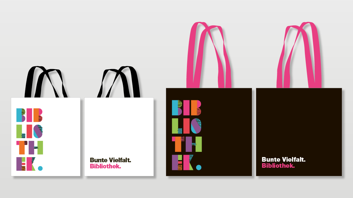 Zwei Bibliothekstaschen in den Grössen klein und gross von beiden ist Vorder- und Rückseite abgebildet. Die kleine Tasche (links) ist weiss mit schwarzen Henkeln und die grosse Tasche (rechts) ist schwarz mit pinken Henkeln. Beide Taschen haben auf der Vorderseite die Aufschrift «Bib-lio-th-ek» in verschiedenen Farben und auf der Rückseite die Aufschrift «Bunte Vielfalt.» darunter steht in pink «Bibliothek.»