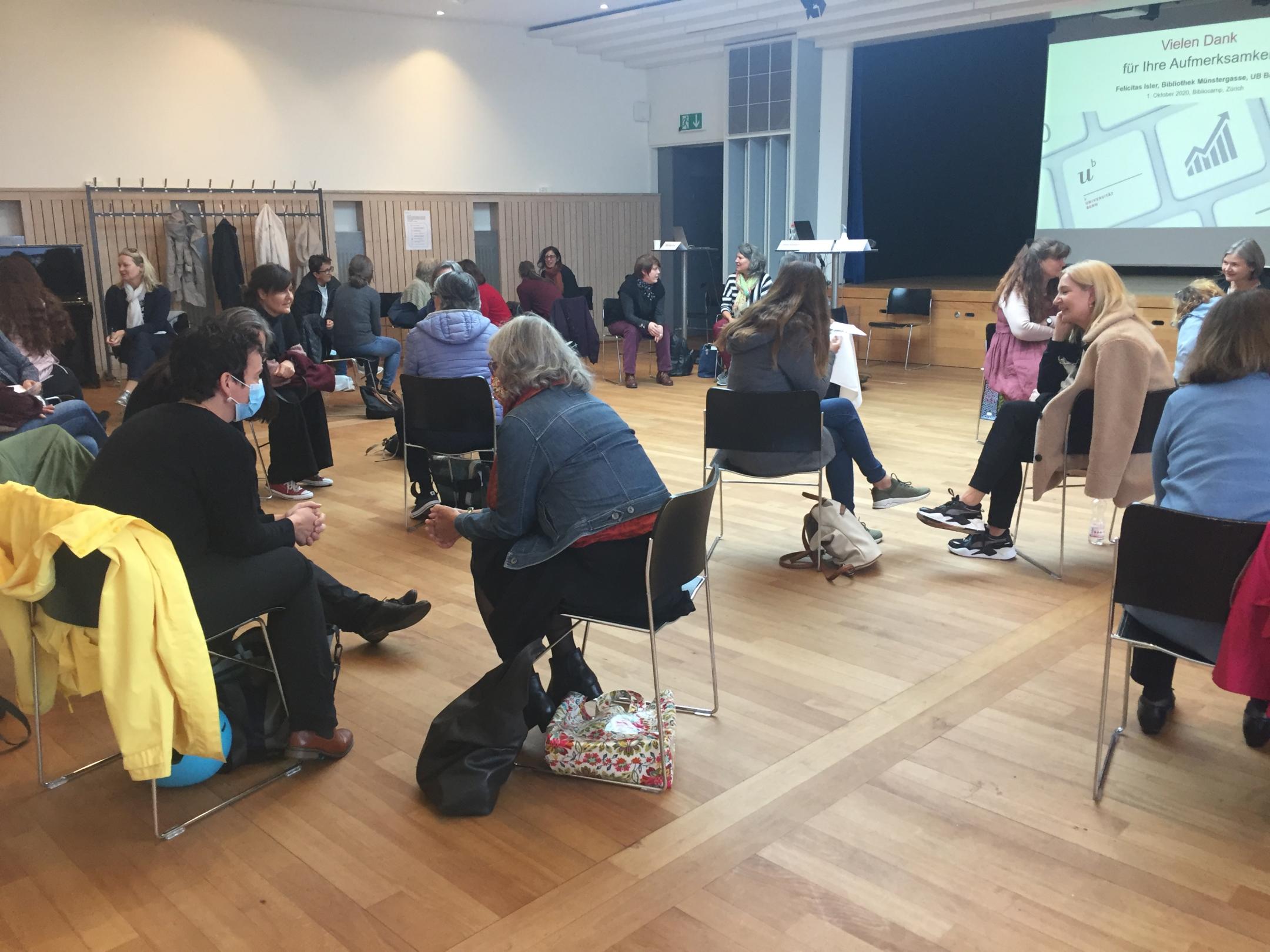 Frauen sitzen in einem Saal und diskutieren immer zu zweit miteinander. In der rechten oberen Ecke sieht man die Projektion der Präsentation.