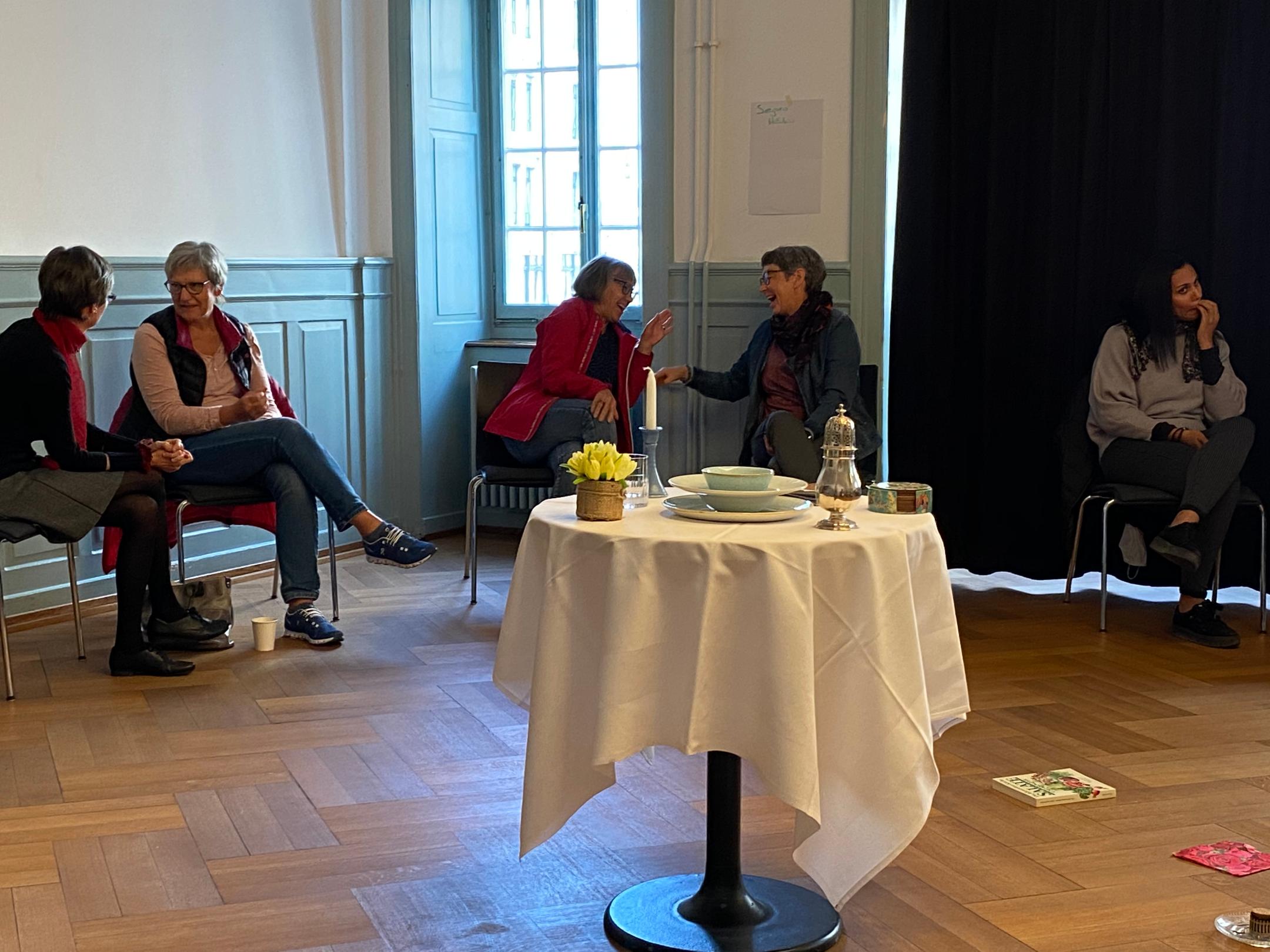 Im Vordergrund steht ein weiss gedeckter Tisch. Dahinter diskutieren Frauen in Zweier-Gruppen.