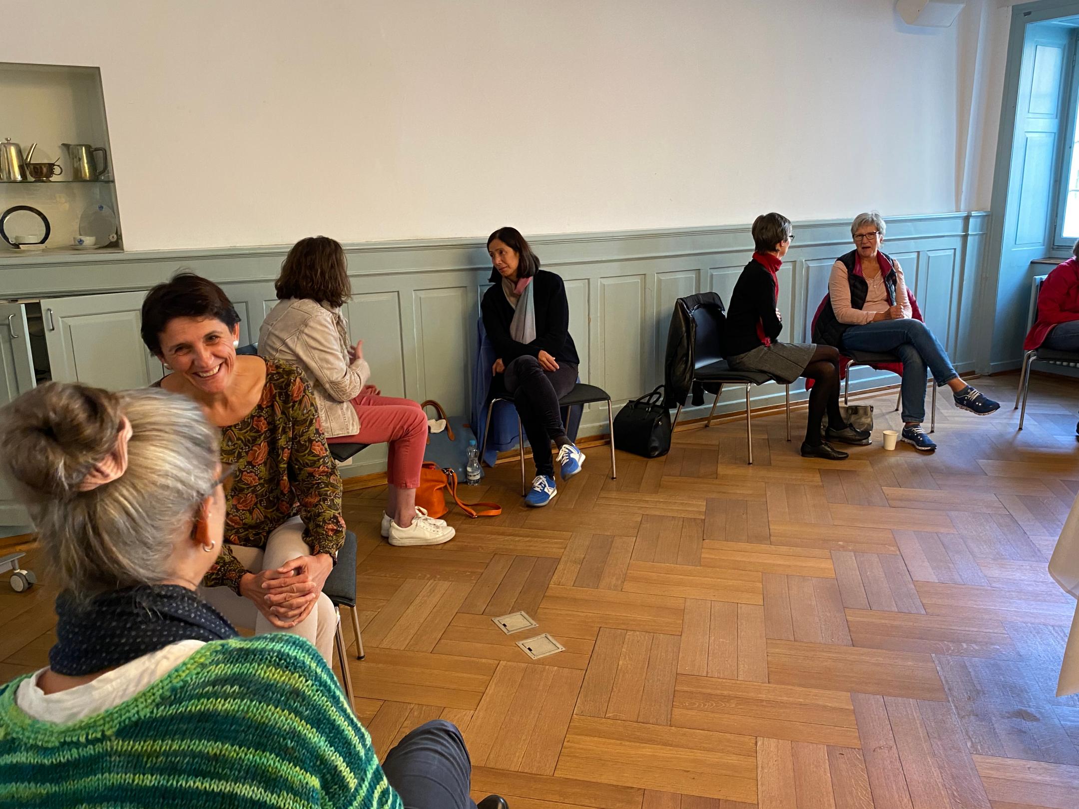 Frauen sitzen in einem Raum den Wänden entlang und diskutieren immer zu zweit miteinander.