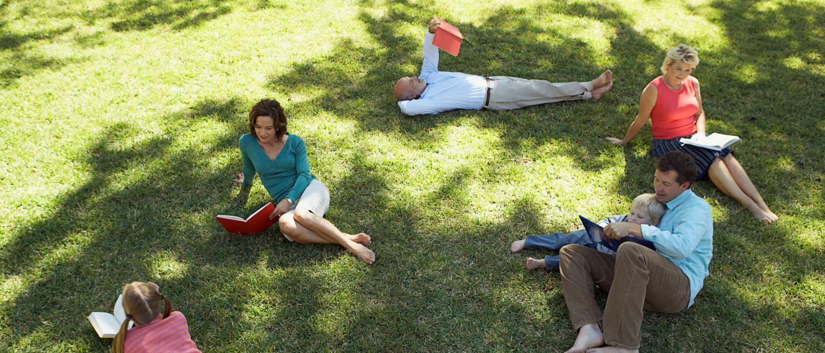 Eine Gruppe Leute liegen auf einer Wiese und lesen ein Buch.