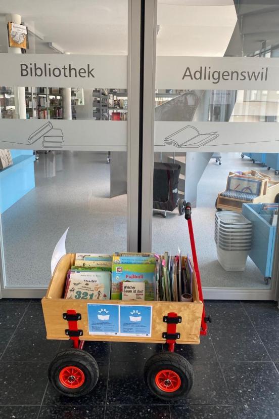 Ein mit Büchern gefüllter Leiterwagen steht vor einer Bibliothek.