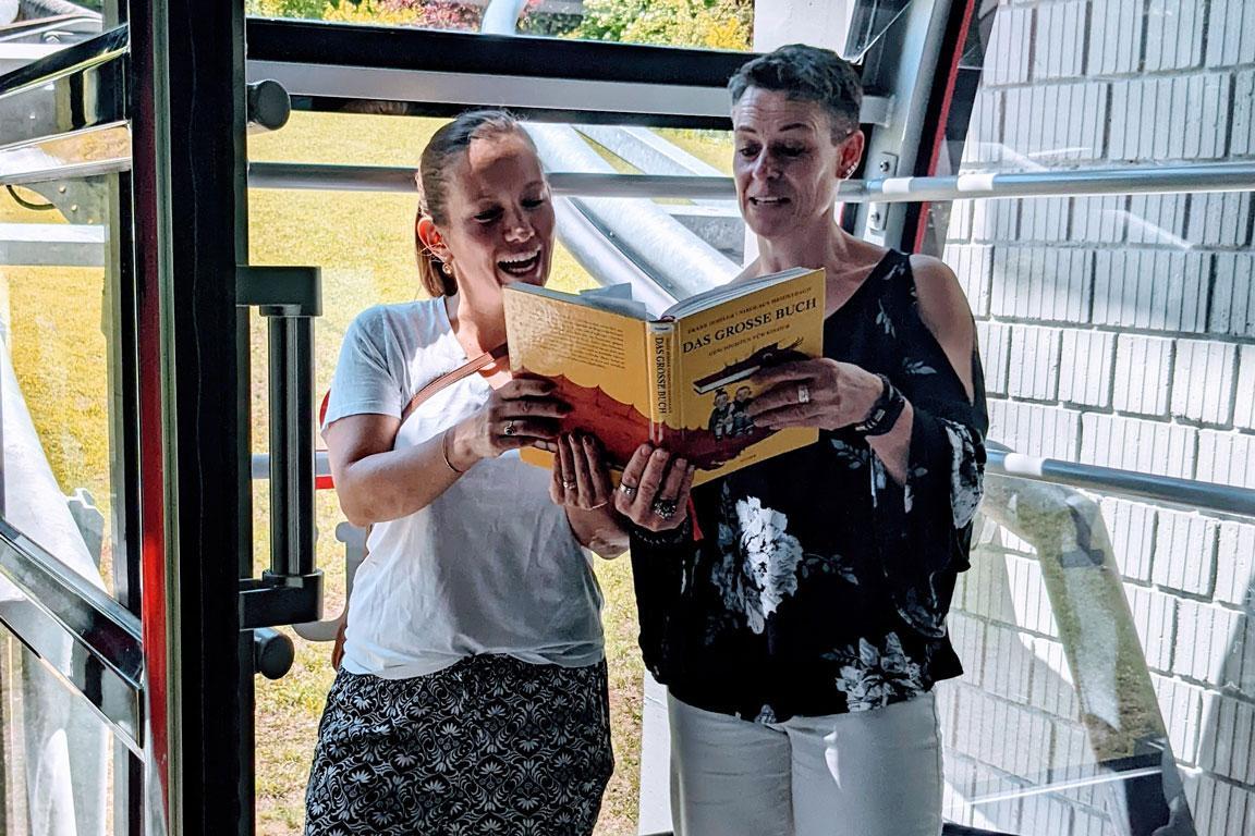 Zwei Frauen lesen aus einem Buch vor.