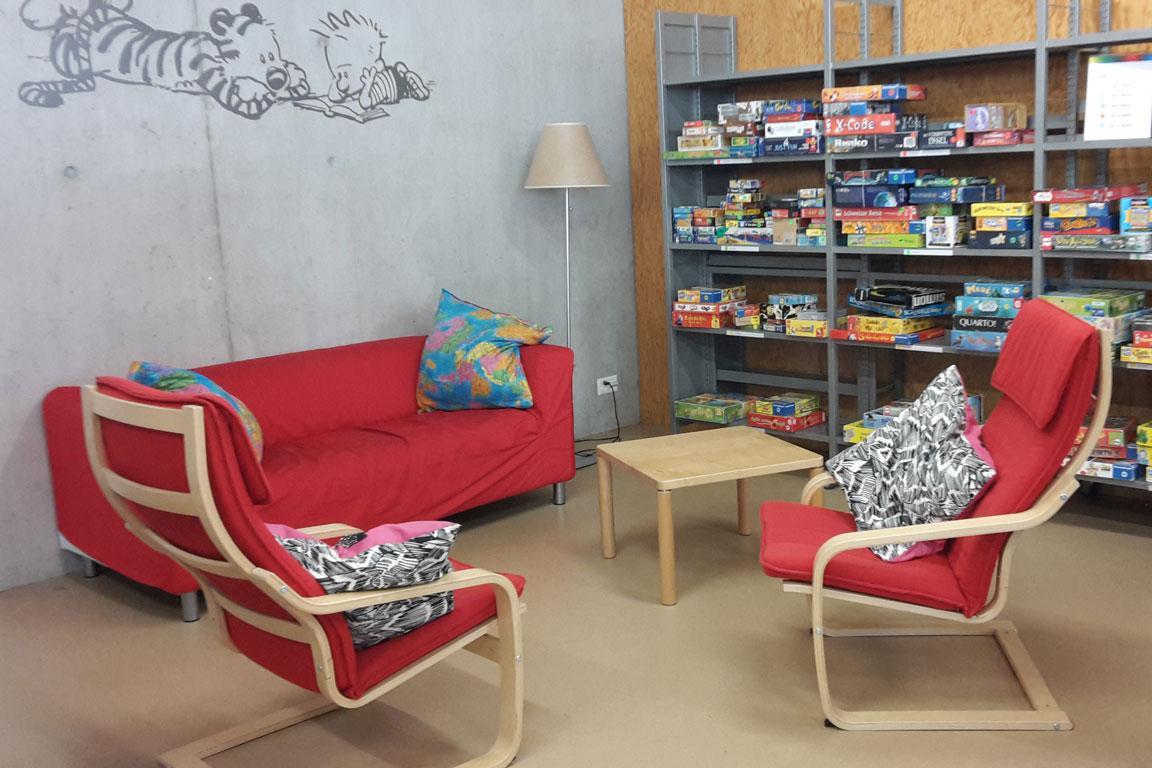 In einer Bibliothek steht ein rotes Sofa und zwei Stühle mit roten Polstern um einen kleinen Holztisch.