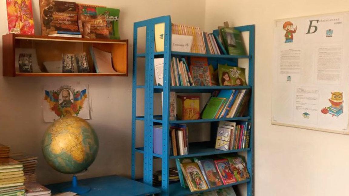 In einem Raum der Dorf- und Schulbibliothek in Putylovychi (Ukraine) steht ein Regal mit Büchern. Daneben steht auf einem Tischchen eine Weltatlas-Kugel.