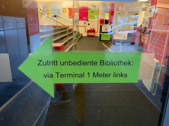 Grüner Hinweispfeil an Glasscheibe weist auf den Zutritt zur unbedienten Bibliothek Uster hin.
