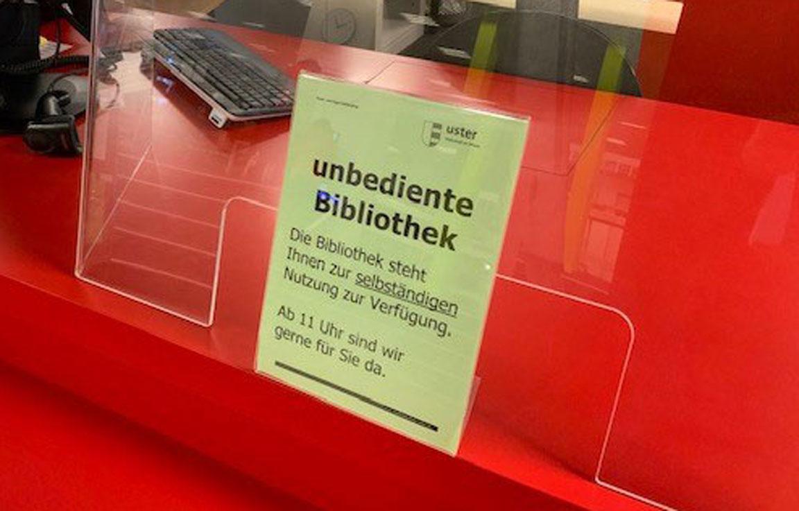 Auf einem grünem Flyer vor rotem Schalter wird auf die unbediente Bibliothek Uster hingewiesen.