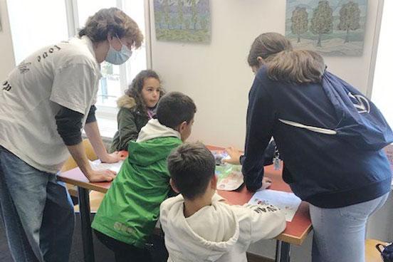 Mehrere Kinder und eine Frau verfolgen gespannt einen Blue-Bot.