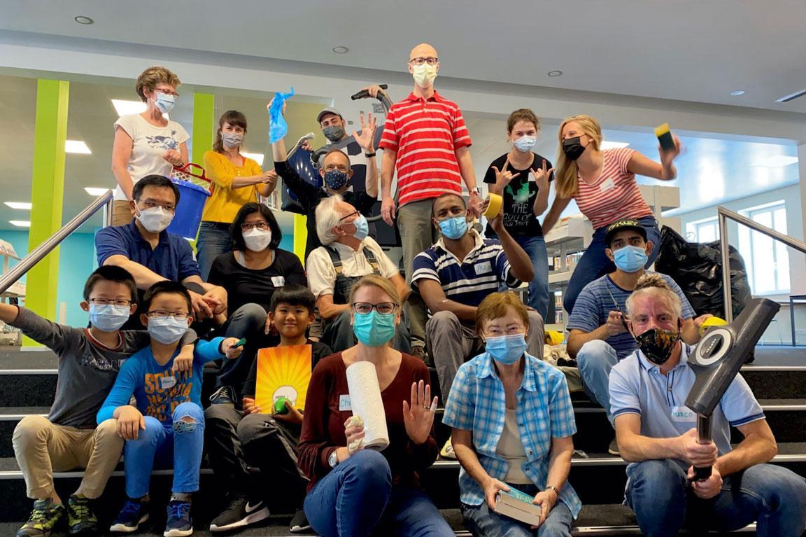 Mehrere Personen mit Schutzmasken sitzen auf einer Treppe.