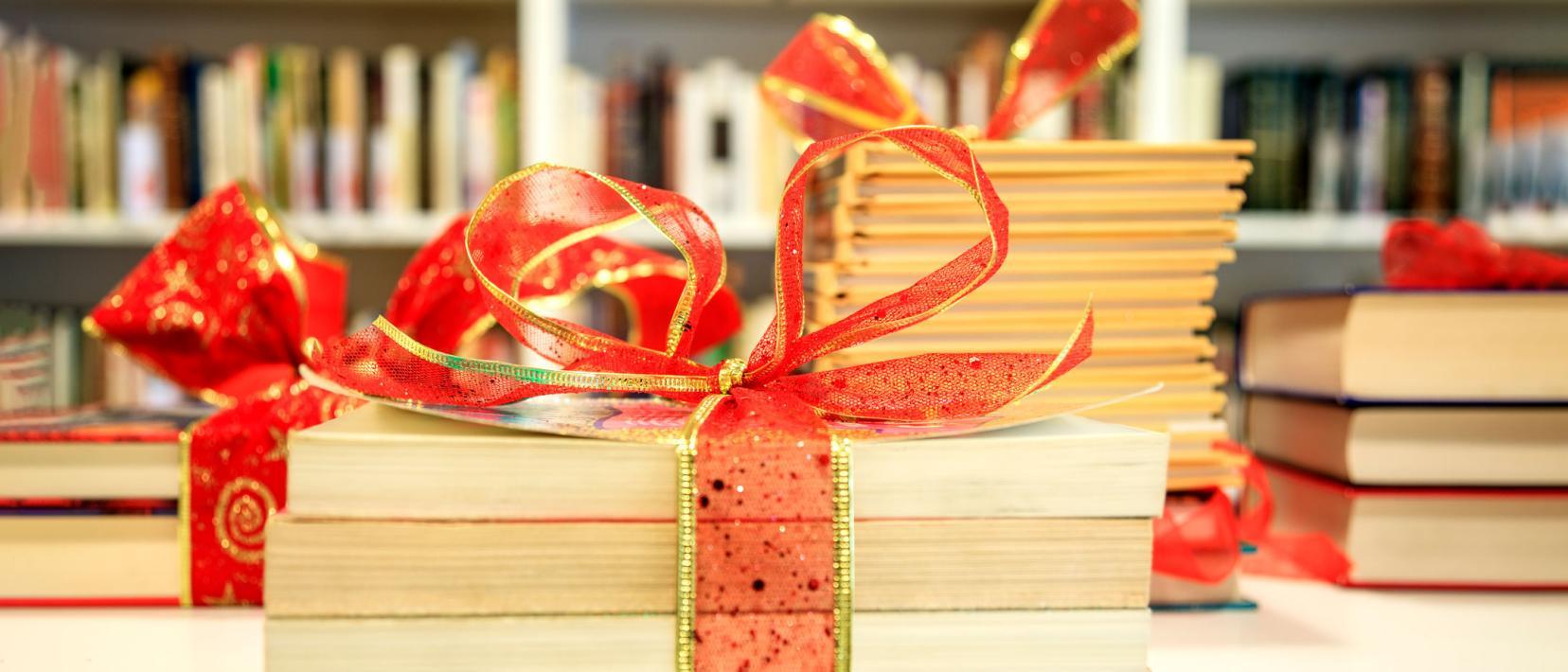 Bücher mit rotem Weihnachtsband zusammengebunden liegen auf einem Tisch vor einer Bücherwand.