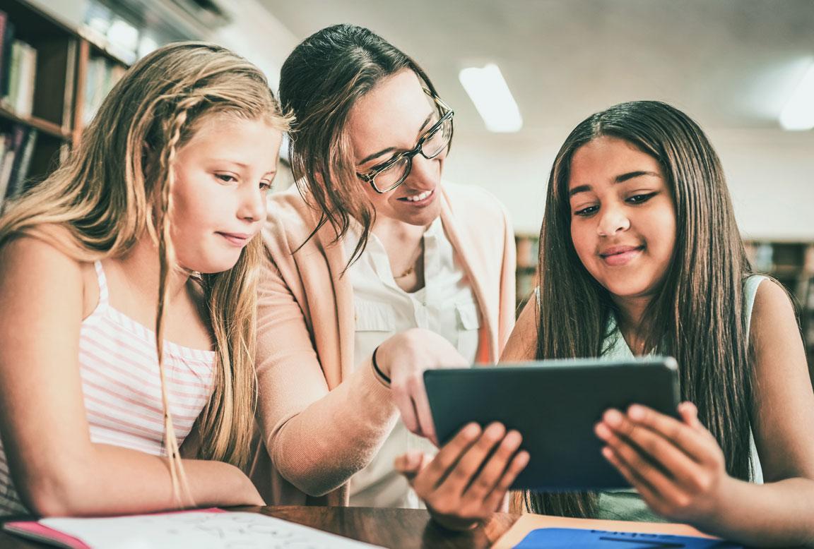 Eine Bibliothekarin schaut mit zwei 12-jährigen Mädchen ein E-Book auf einem  Tablet an.