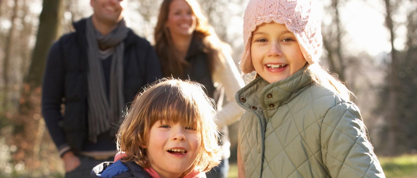 Zwei Kinder lachen, hinter ihnen stehen zwei Erwachsene Personen