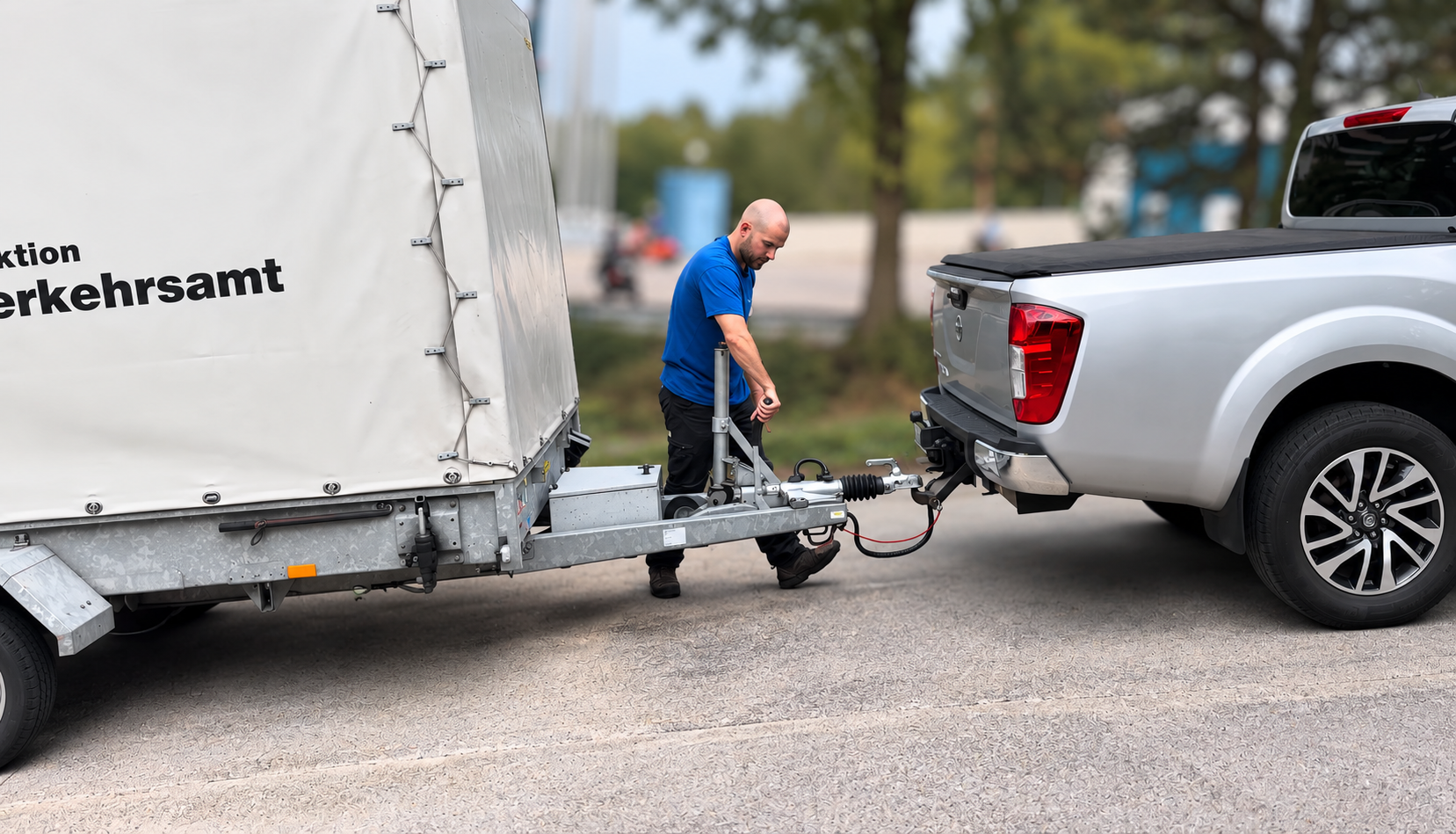 Ein Mitarbeiter kuppelt einen Planenanhänger mit der Aufschrift «Strassenverkehrsamt» an einen silbernen Pick-up an.