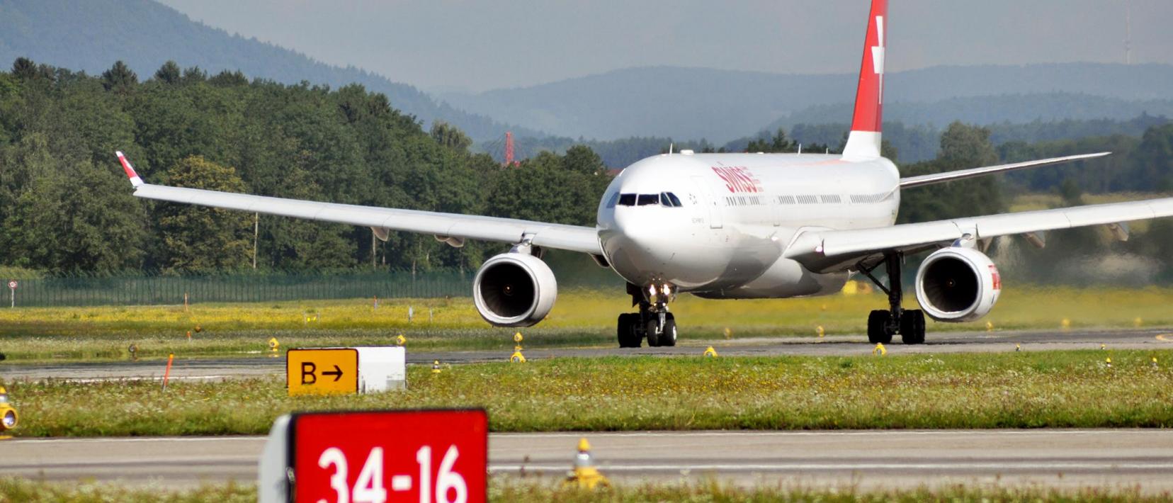 Das Bild zeigt ein Flugzeug der Swiss am Flughafen Zürich mit Wald im Hintergrund.