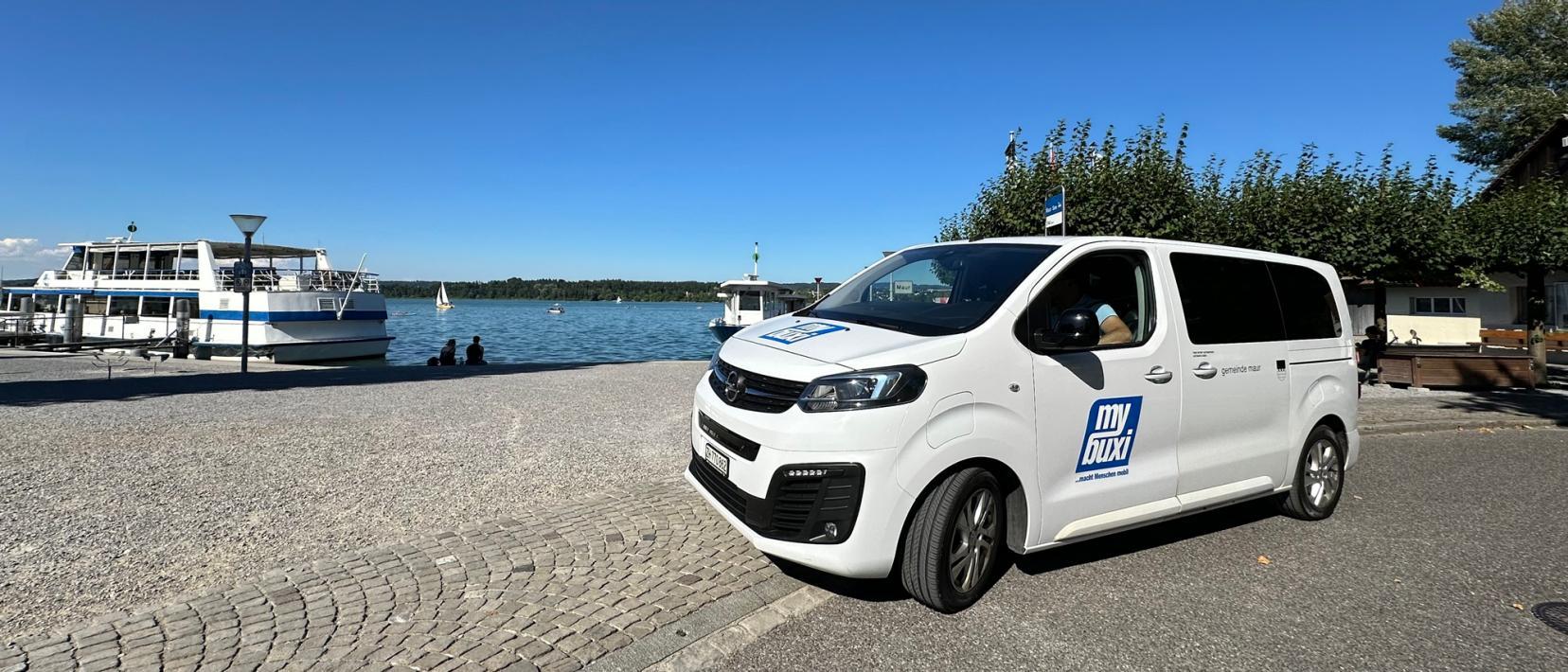 Ein Bus mit Aufschrift «MyBuxi» steht vor einem Schiffsanleger am Greifensee