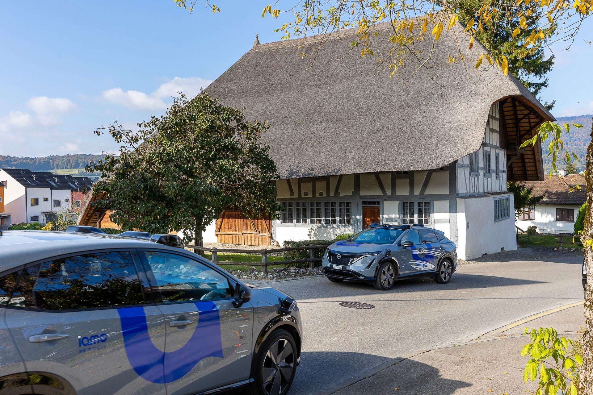 Zwei selbstfahrende Fahrzeuge kreuzen sich auf einer Landstrasse im zürcherischen Furttal vor dem Strohdachhaus im zürcherischen Hüttikon. 