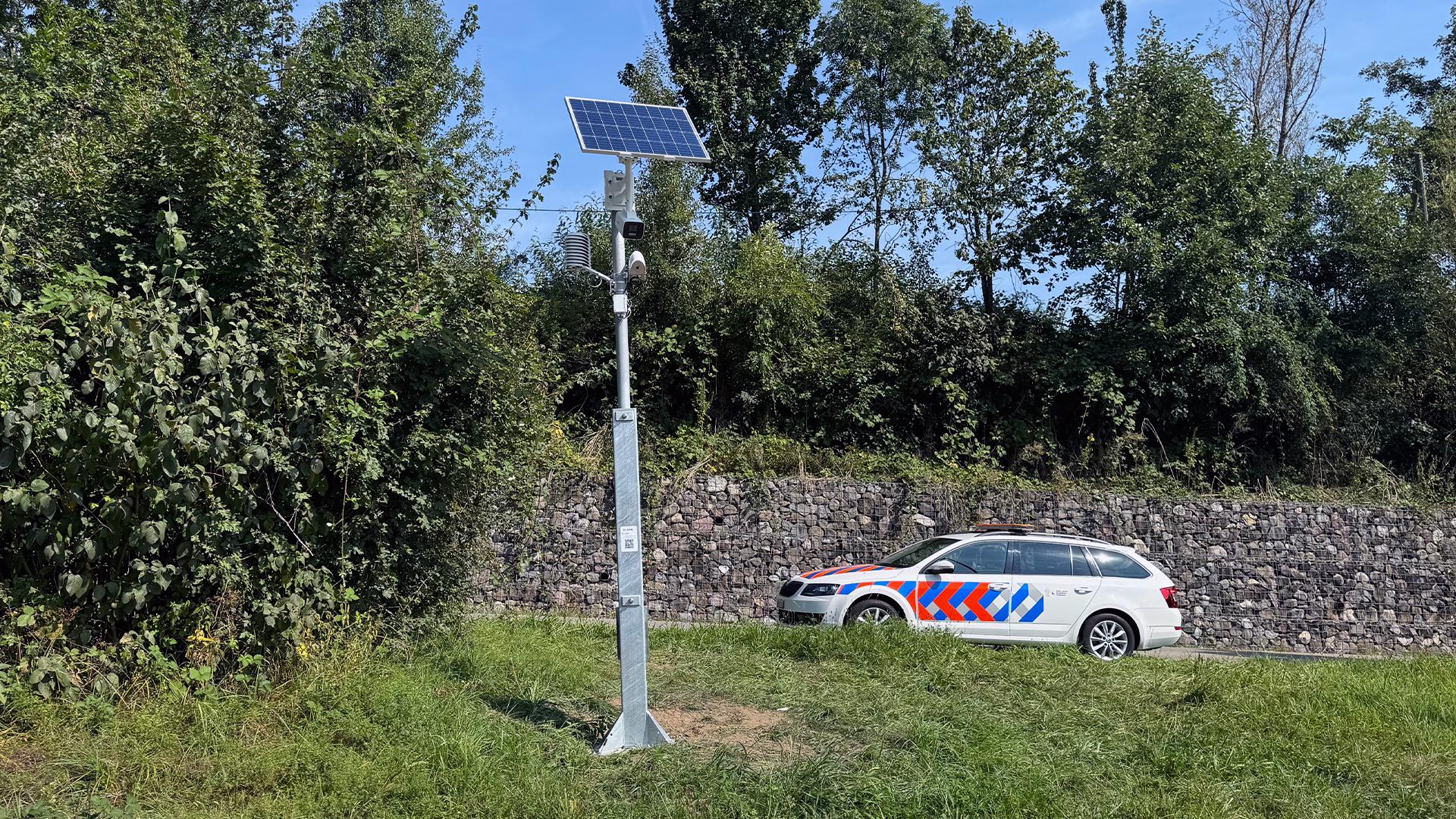 Frühwarnanlage mit Solarmodul neben einem Auto und einer Steinmauer.