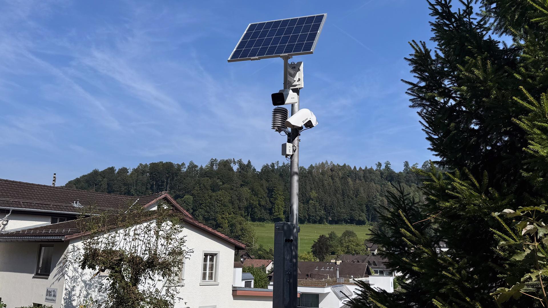 Detailaufnahme der solarbetriebenen Frühwarnanlage auf einem Mast über Hausdächern.