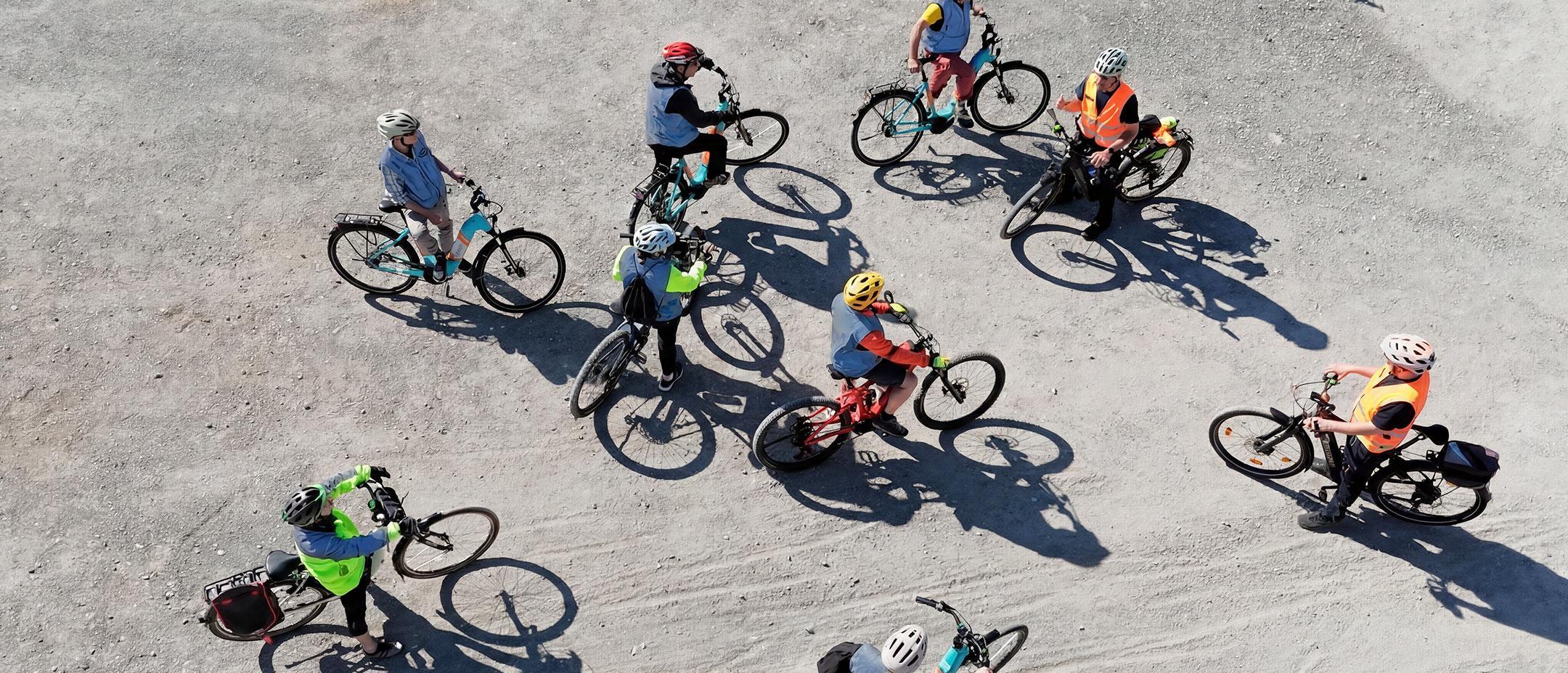 Drohnenansicht einer Gruppe von Radfahrern mit bunten Helmen und Warnwesten auf einem Schotterweg.