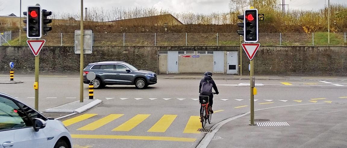 Eine Ampel mit rotem Licht für Fahrräder. Unter der Ampel ist ein «Vortritt gewähren»-Schild und ein kleines Schild mit einem Fahrradsymbol und einem nach rechts zeigenden Pfeil.