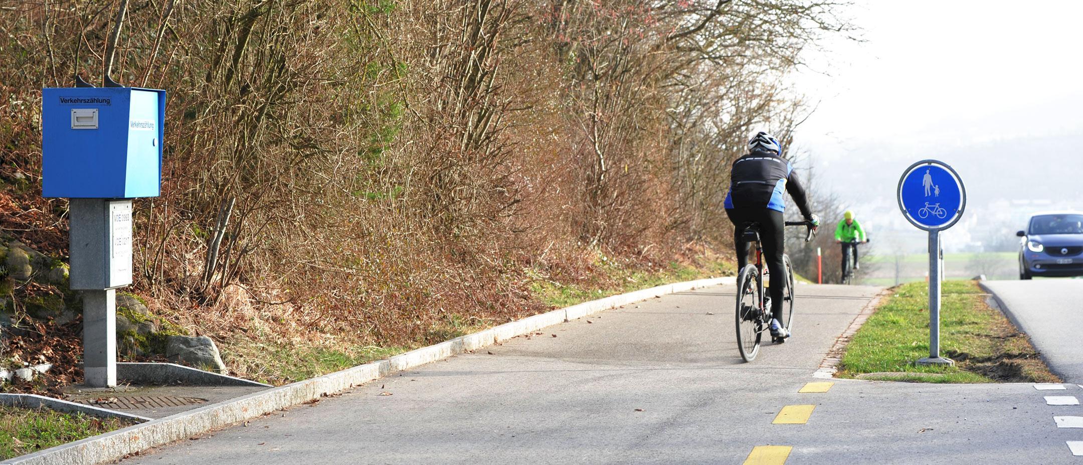 Velofahrer fährt an einer blauen Box vorbei. Diese steht am Rande eines separat geführten Veloweges.